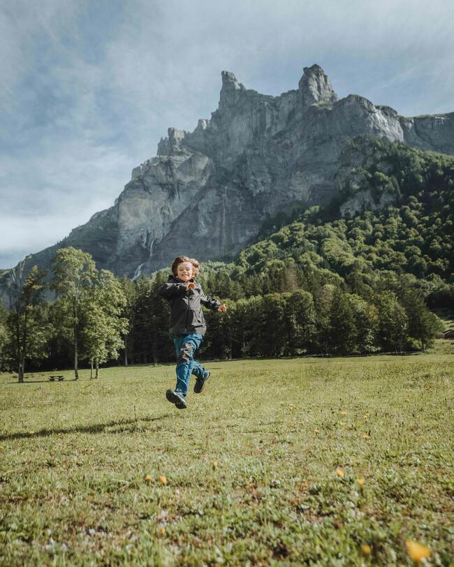 Kind rennt auf einer Wiese in den Bergen