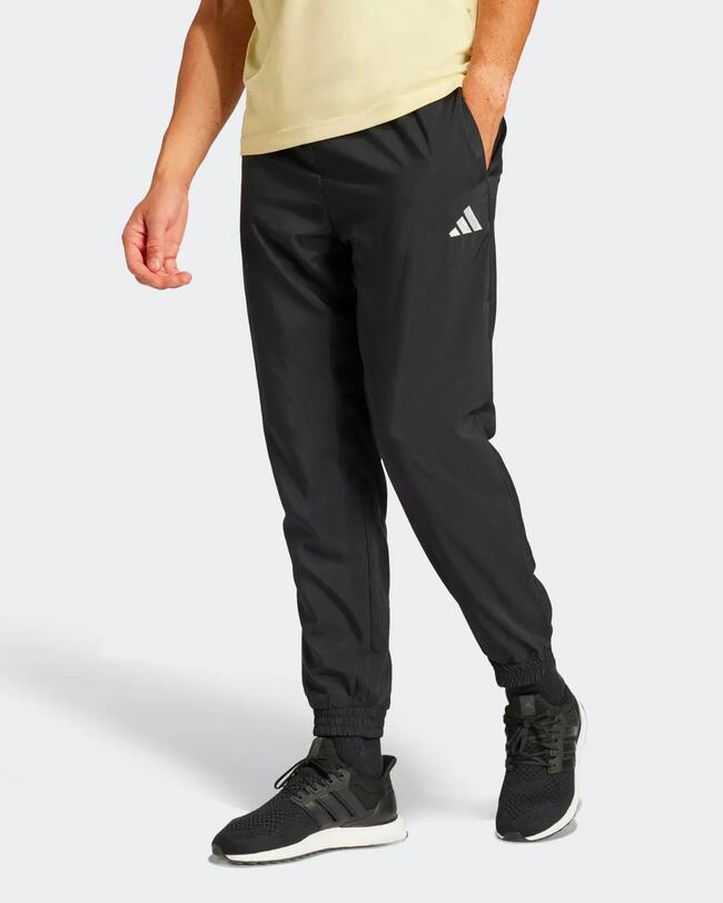 Mann trägt schwarze Adidas-Trainingshose mit Bündchen, weißem Logo und gelbem T-Shirt.