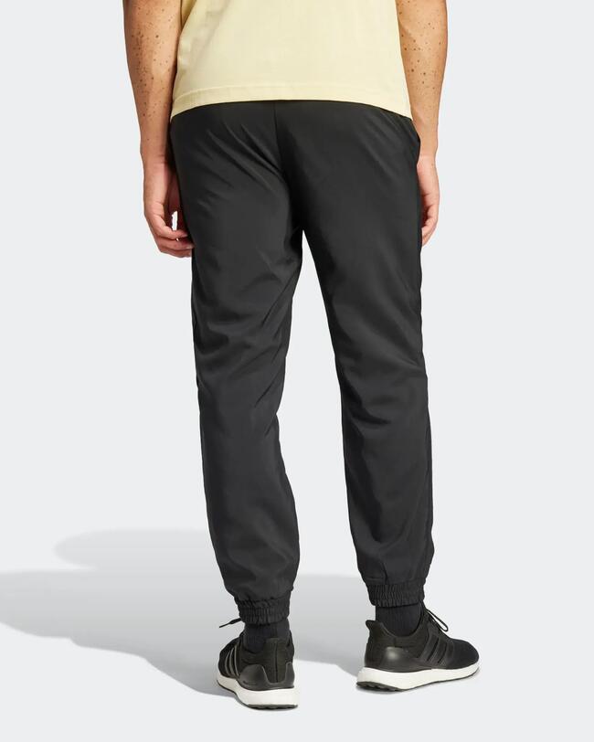 Rückenansicht eines Mannes in schwarzer Adidas-Trainingshose mit Bündchen und gelbem T-Shirt.