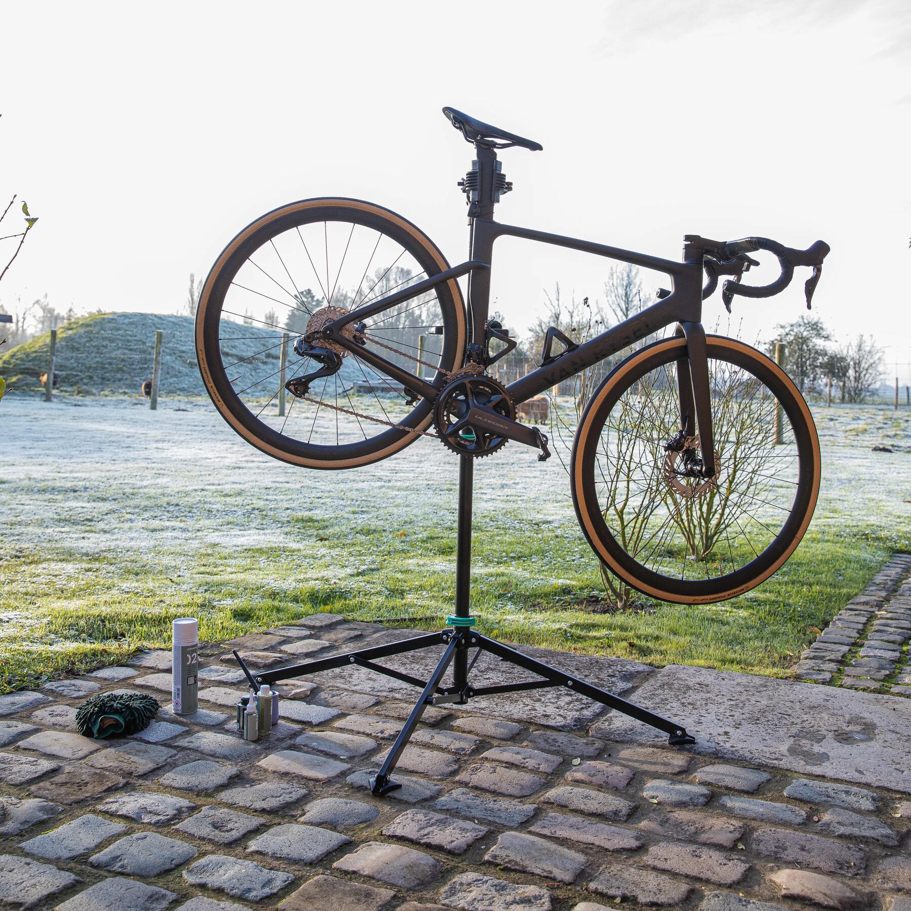 A bike on a repair stand outside next to cleaning products