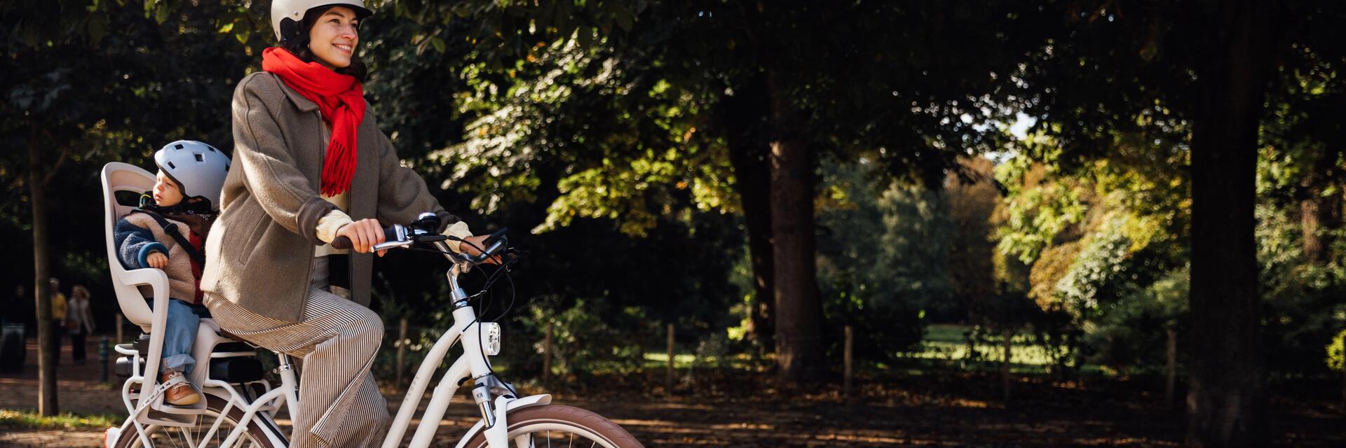 Mama w kasku przewożąca dziecko na rowerze w kasku w foteliku rowerowym