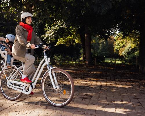 Mama w kasku przewożąca dziecko na rowerze w kasku w foteliku rowerowym