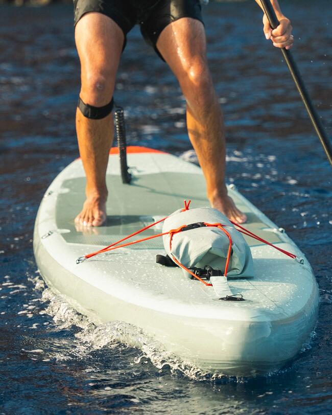 Person paddelt auf einem hellgrauen Stand-Up-Paddle-Board über blaues Wasser. Spritzendes Wasser, sonnige Beleuchtung.