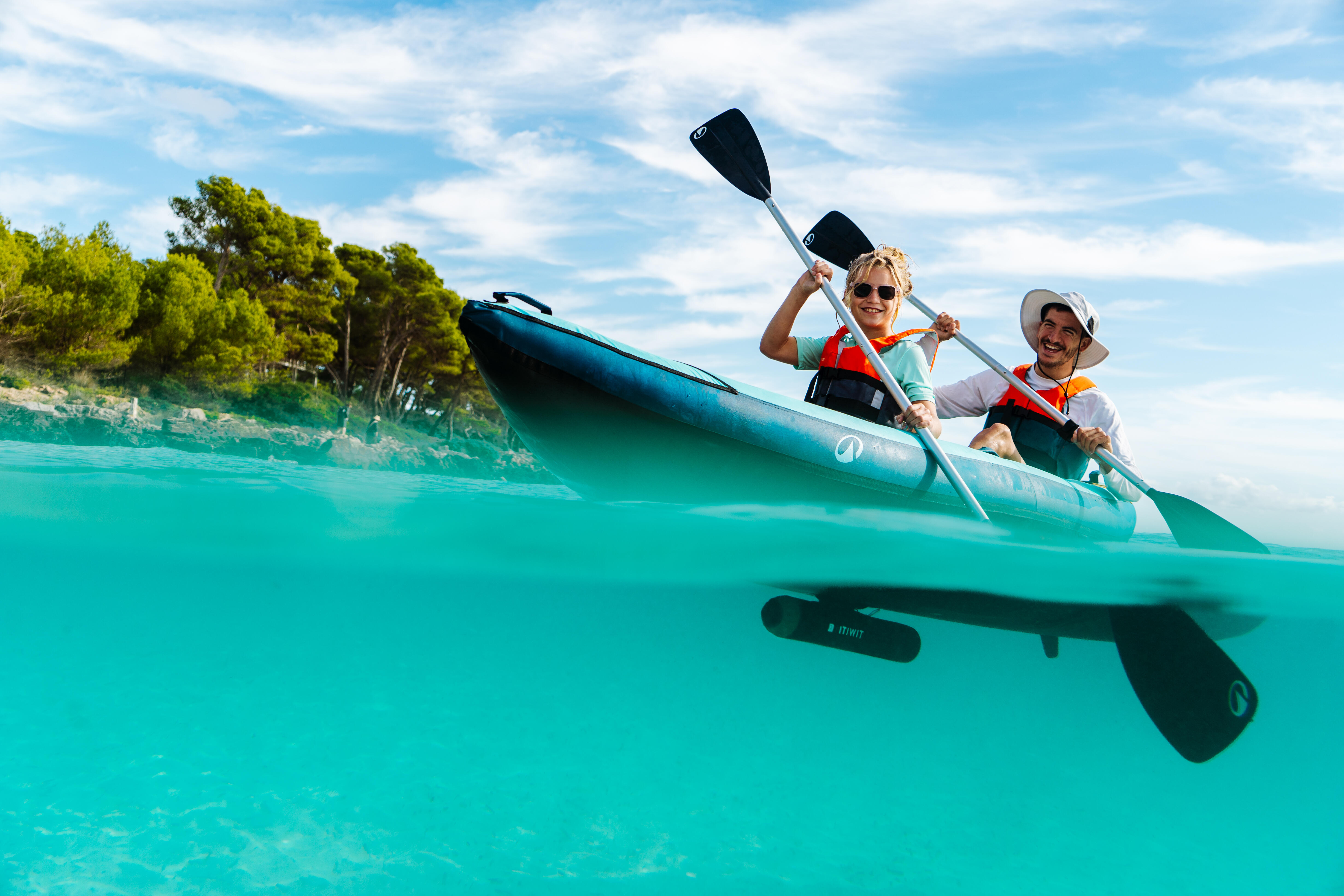 Adult and child paddling an inflatable kayak in clear coastal water