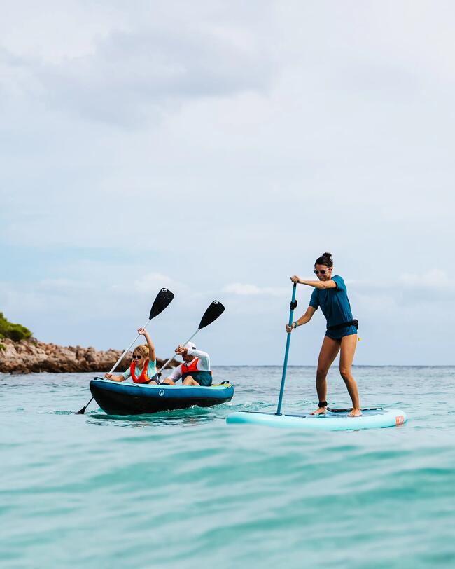 Drei Personen auf türkisfarbenem Meer beim Kajakfahren und Stand-Up-Paddling unter teils bewölktem Himmel.