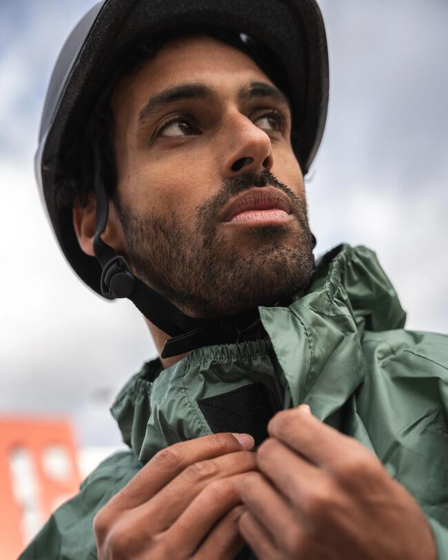Mann mit Helm, grüne Jacke, blickt nachdenklich nach oben, bewölkter Himmel im Hintergrund, Kontraste in Braun und Grün.