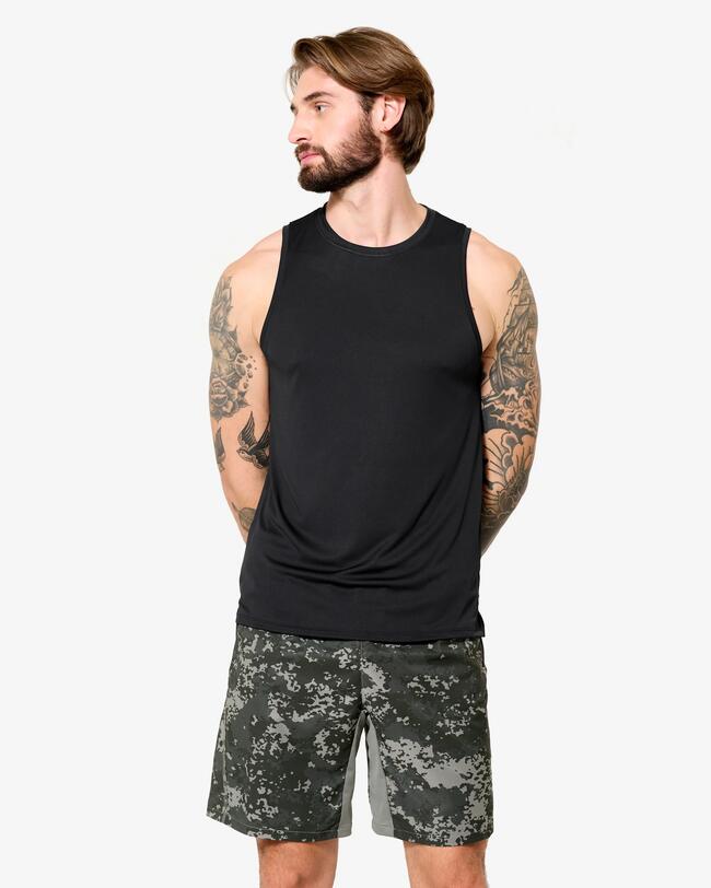 Männliches Model in schwarzem Tanktop und Tarnmuster-Shorts posiert vor einem weißen Hintergrund.