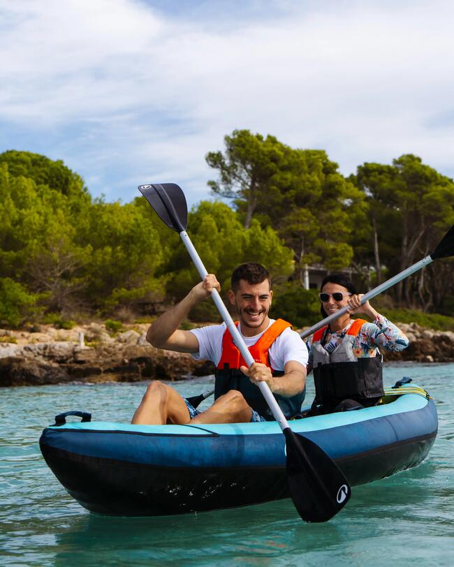 Zwei Personen im blauen Kajak auf türkisblauem Wasser, umgeben von grünen Bäumen und Wolken am Himmel.