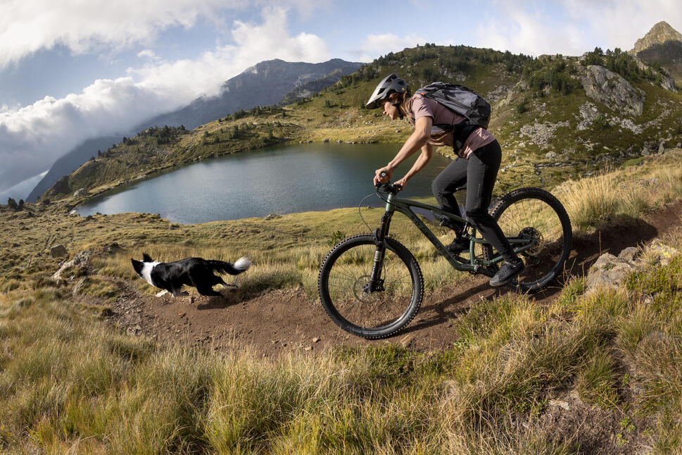 Ženska na gorskem kolesu z nahrbtnikom se vozi po ozki gorski poti.