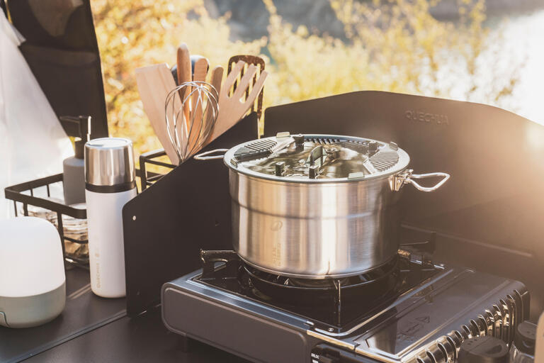 Stainless steel camping cookware set on a portable camping stove at an outdoor campsite