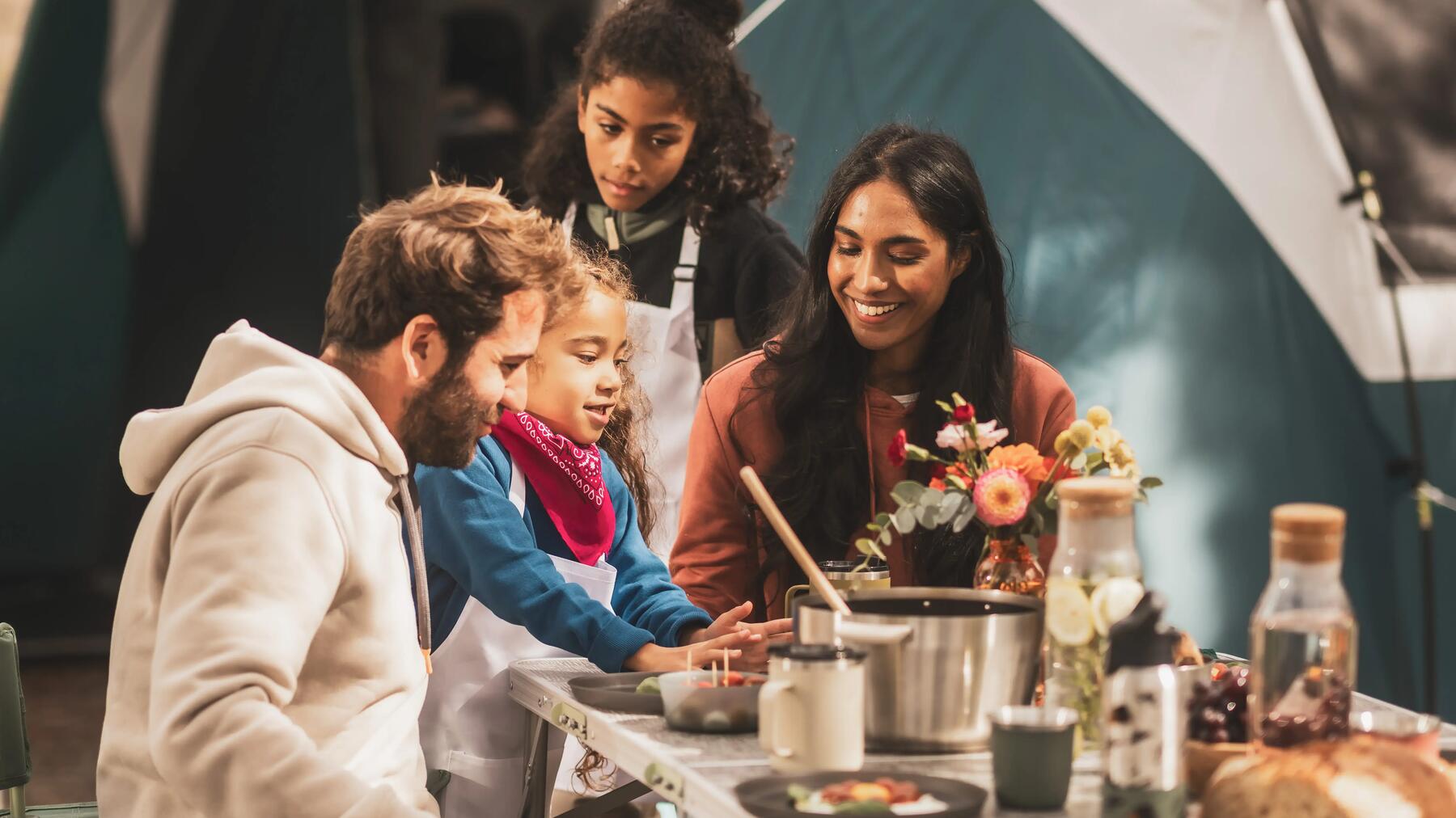 Familie sitzt am Campingtisch vor ihrem Campingzelt.