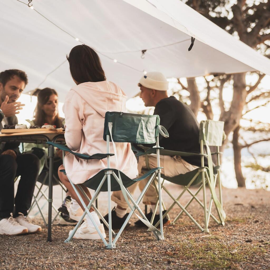 Štirje prijatelji sedijo za zložljivo mizo v Quechua kamping stolih pod belo tendo na obali jezera.