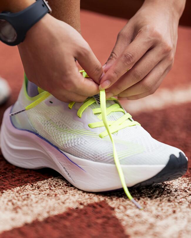 Weiße Laufschuhe mit gelben Schnürsenkeln, Hände binden Schleifen, roter Untergrund, sportlich, dynamisch, modern.