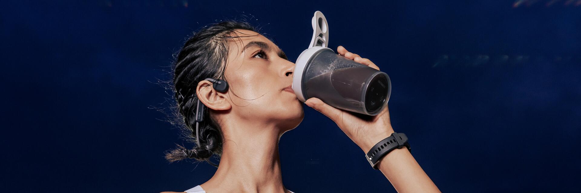 Een vrouw die een sportdrank drinkt uit een shaker van Decathlon