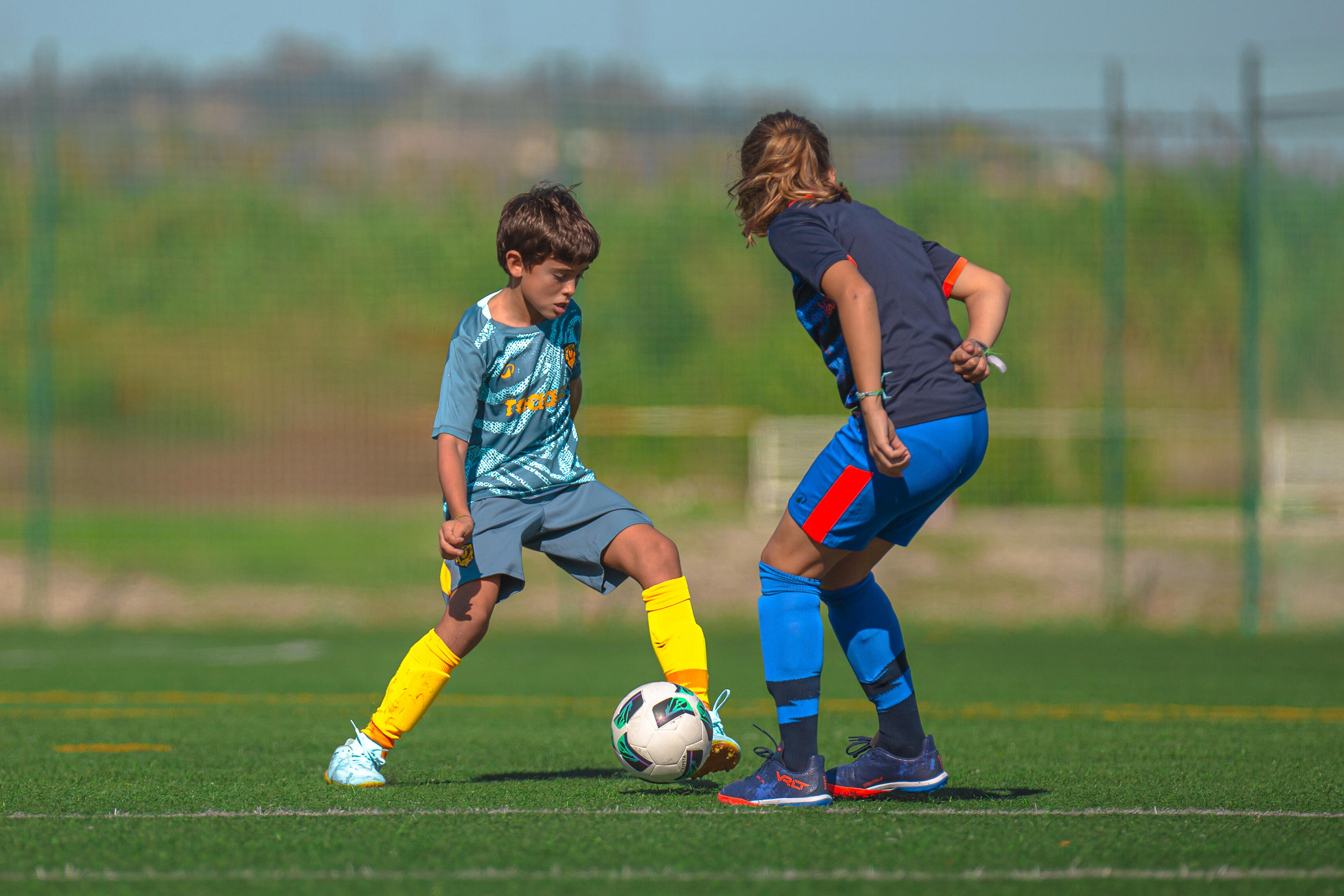 Two children challenging for the ball on a football pitch