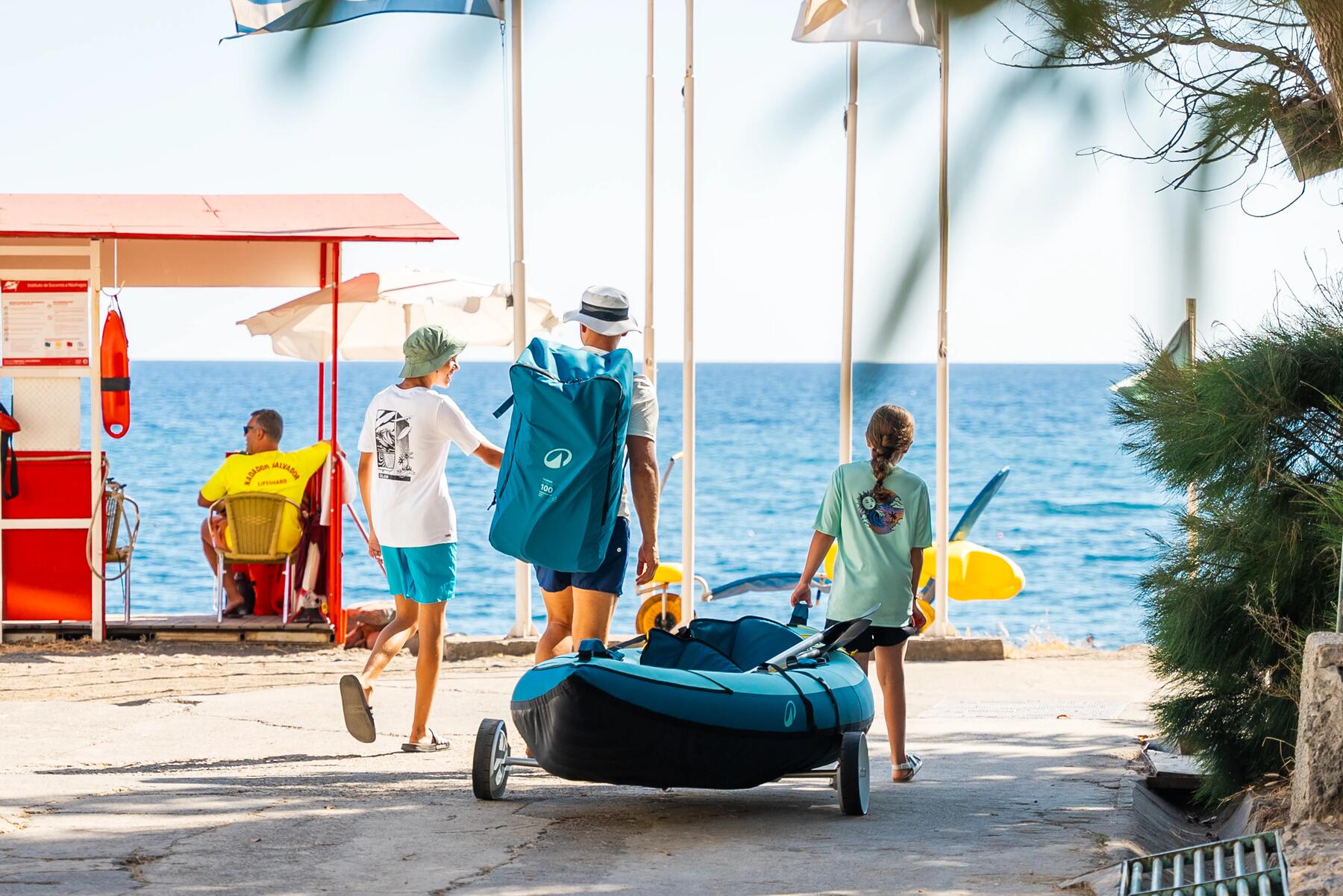 EIn Mann trägt Kajak und Paddel mit seinen Kindern zum Wasser