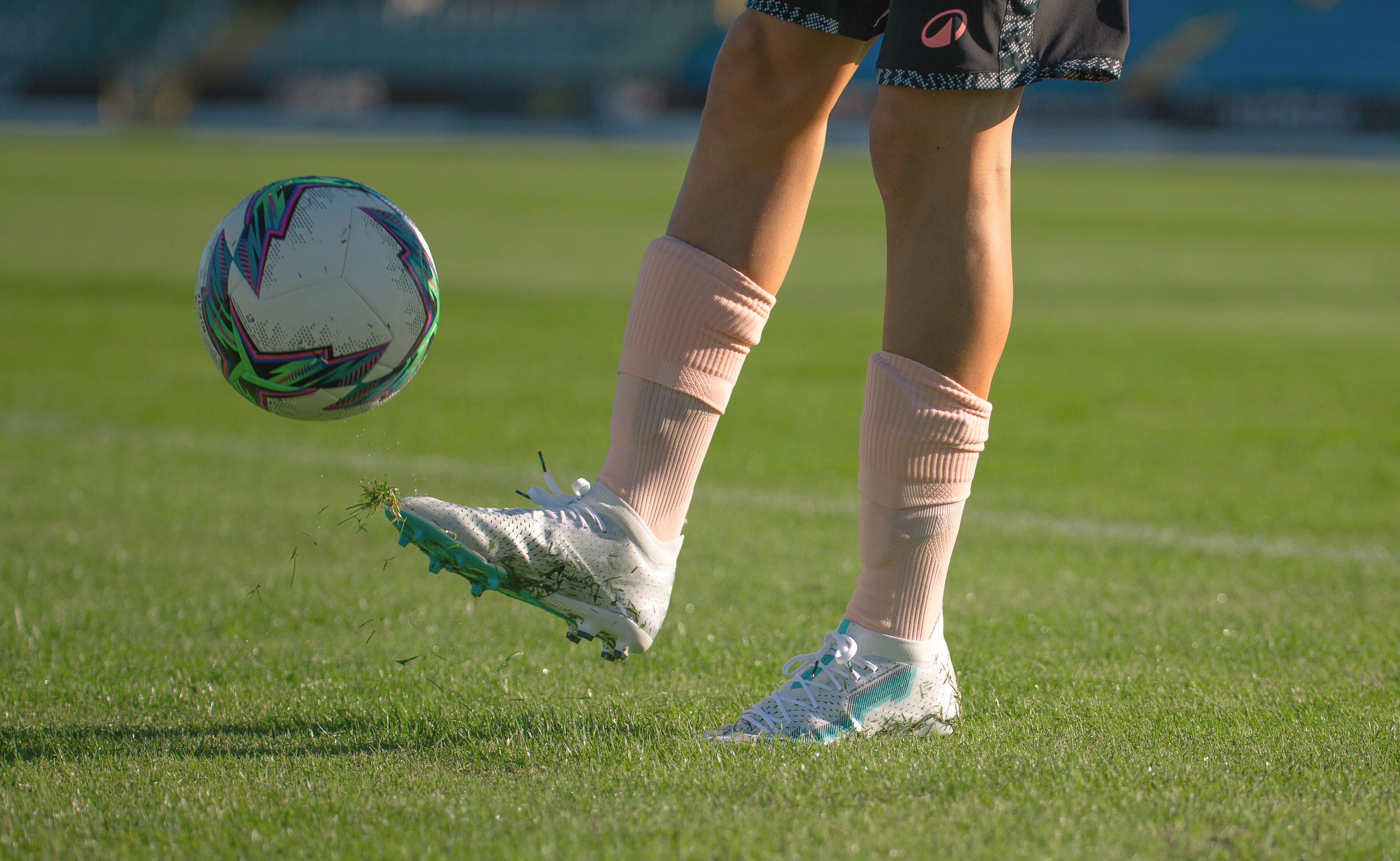 Football player controlling a ball while wearing pink football socks and boots
