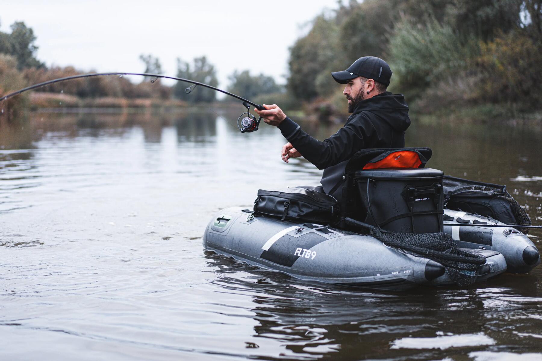 Angler sitzt mit Hund in einem Bellyboot und greift einen Fisch