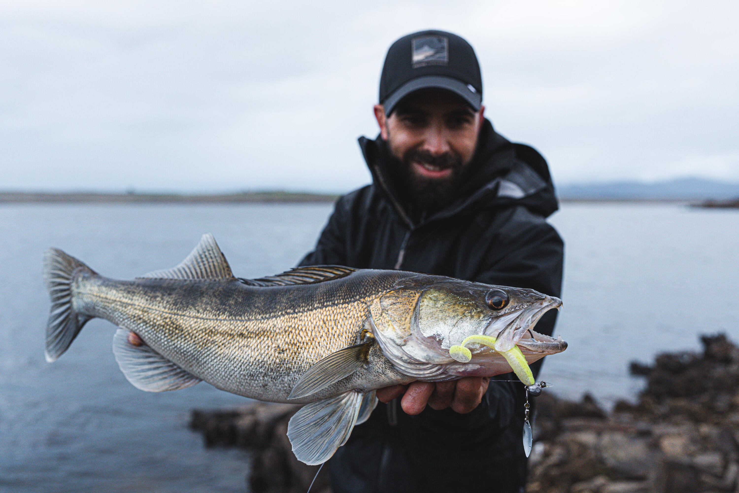 Ein Angler präsentiert einen Zander mit Gummiköder im Maul