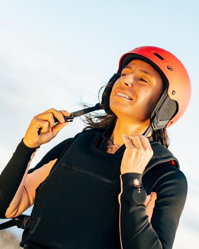 rideuse de wing foil en train d'enfiler son casque d'impact rouge 