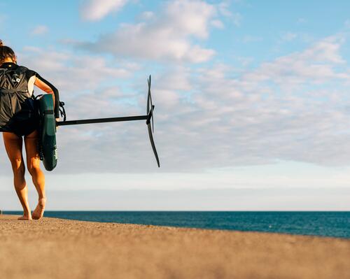 rideuse portant son matériel de wing foil sur la plage