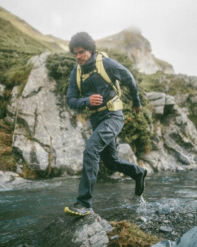 Mann springt im Fluss über einen Stein mit Wanderbekleidung