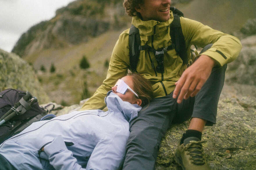 Žena sa naočarima odmara glavu na nogama muškarca tokom predaha na pešačenju u planini.