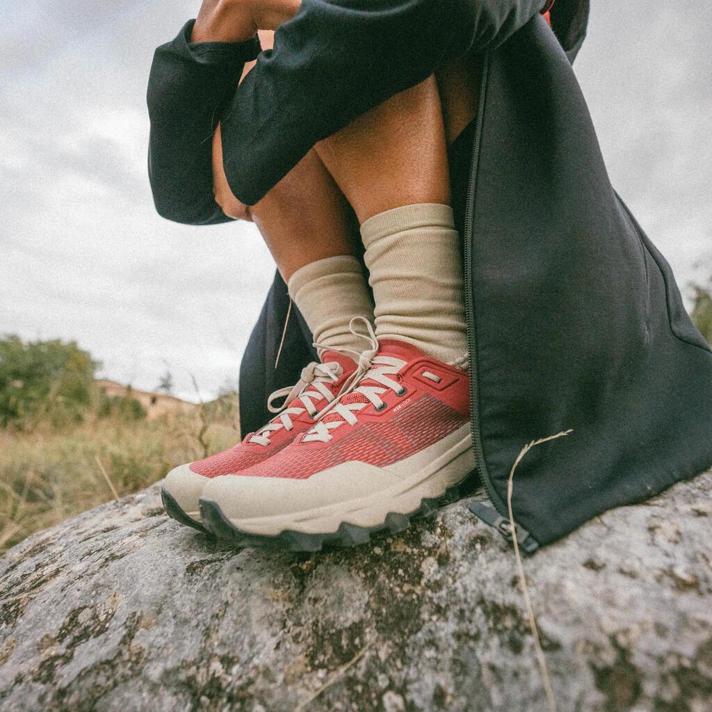 Oseba sedi na skali v rdečih pohodniških čevljih Quechua MH500 Light in bež nogavicah.