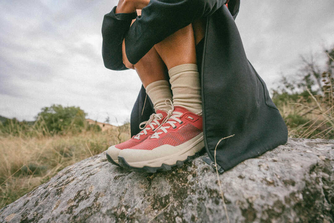 Oseba sedi na skali v rdečih pohodniških čevljih Quechua MH500 Light in bež nogavicah.