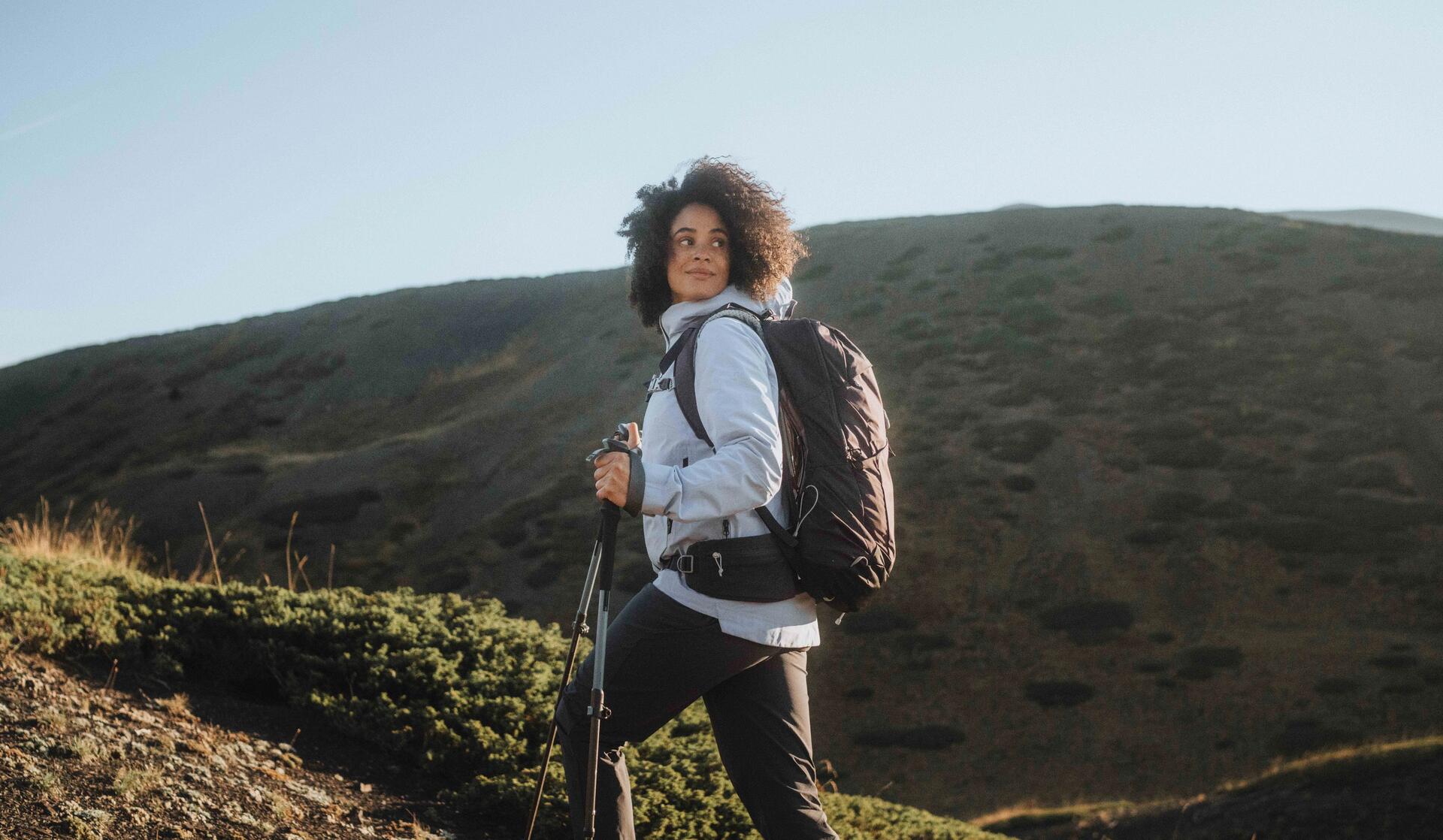 Kobieta w odzieży trekkingowej trzymająca kije trekkingowe wędrując po górach
