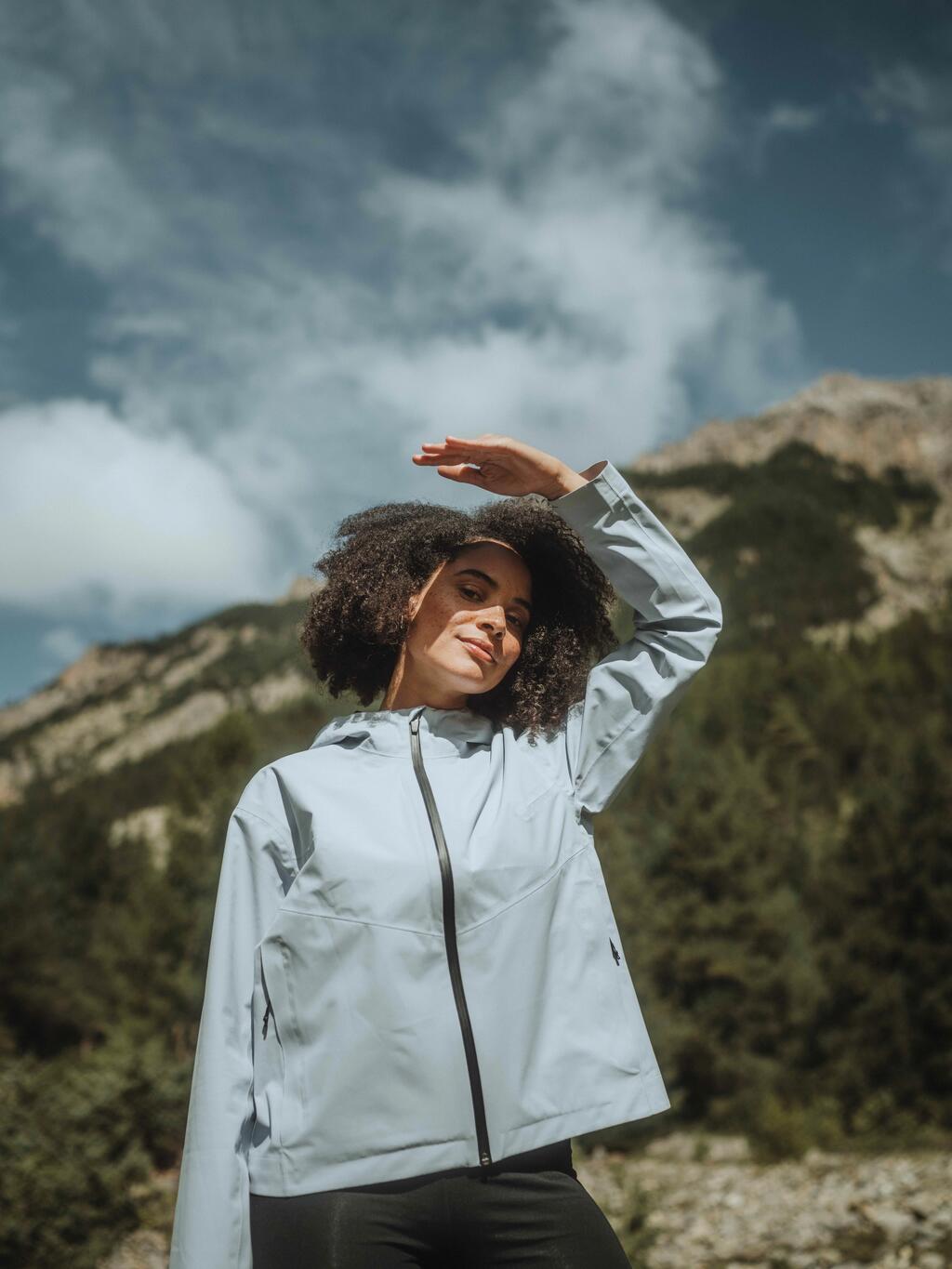 Ženska v svetlo modri jakni pod kamnitim hribom.