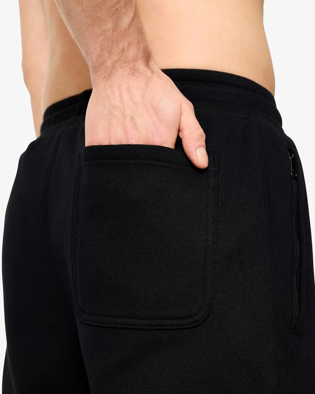 Nahaufnahme der Rückseite einer schwarzen Jogginghose mit einer offenen Tasche, in der eine Hand steckt.