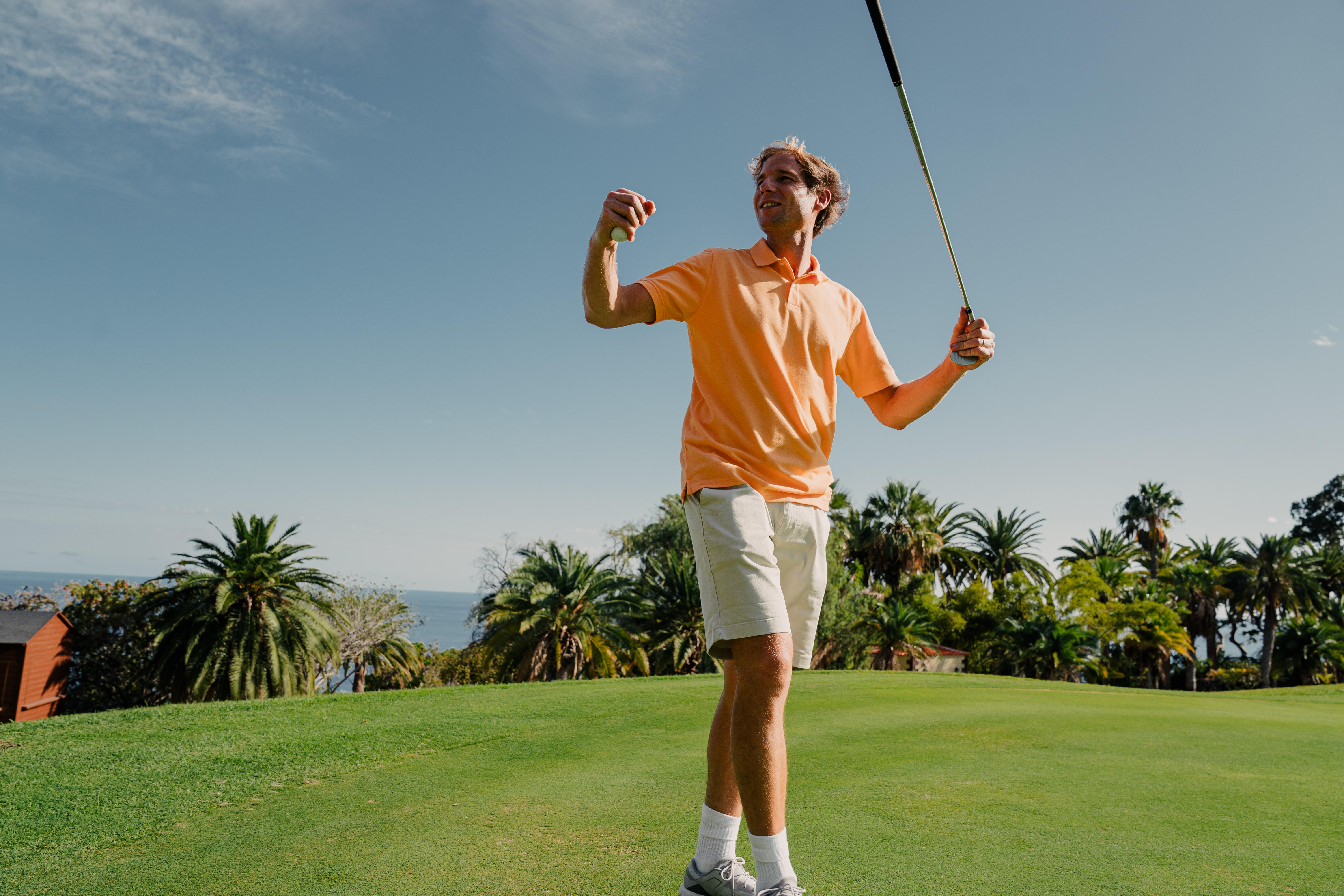 Orange polo shirt and cream shorts worn by a man holding golf club and ball