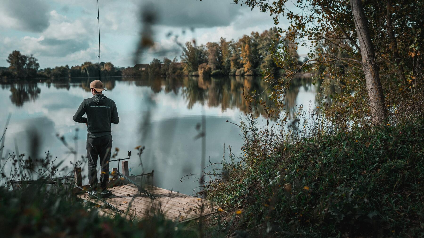 Wędkarz stojący na brzegu jeziora z wędką
