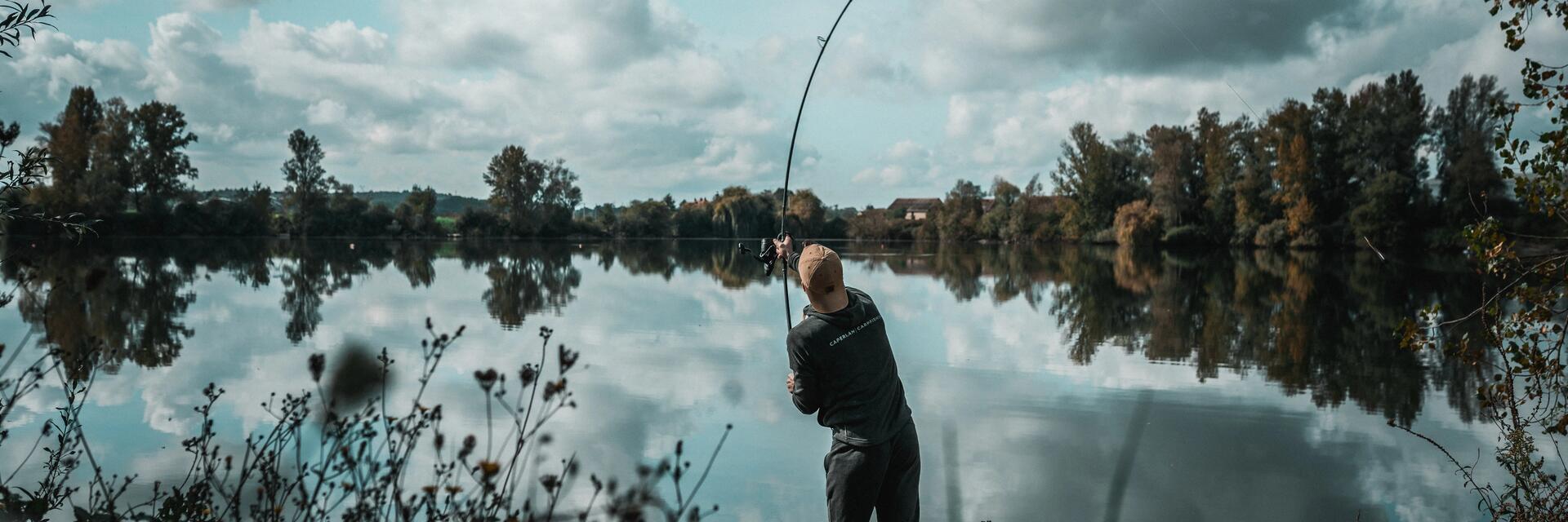 Wędkarz stojący na brzegu stawu zarzucający wędkę do wody
