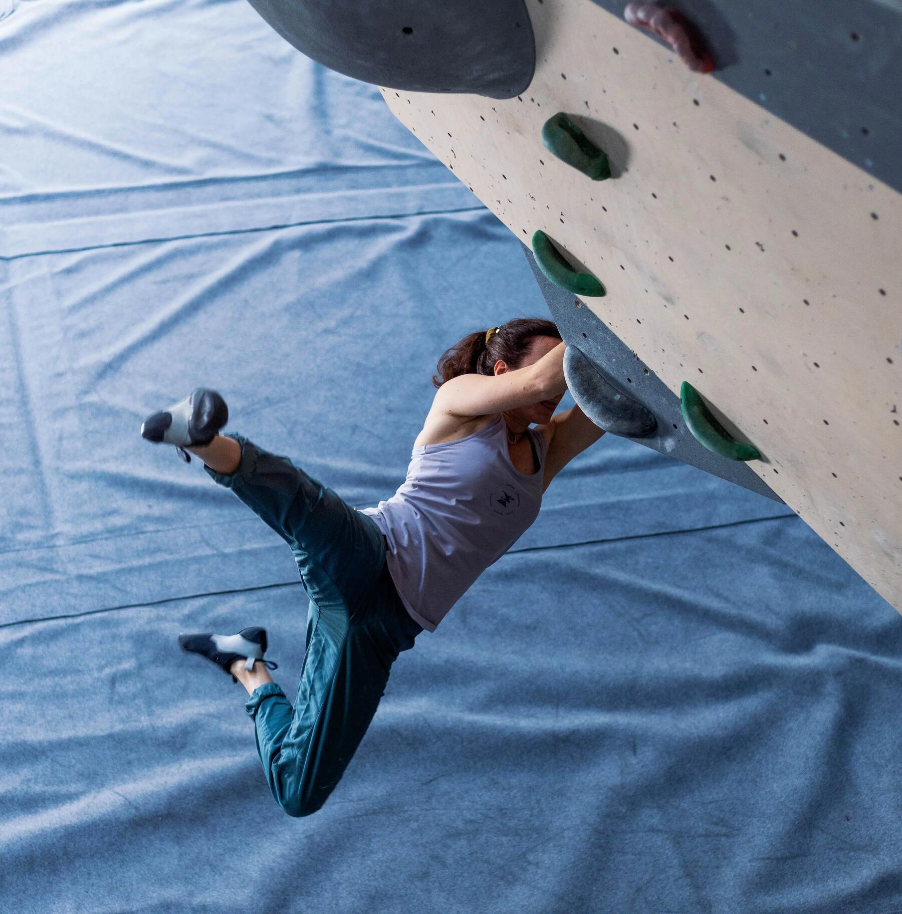 Eine Frau hängt in Boulderschuhen an der Kletterwand