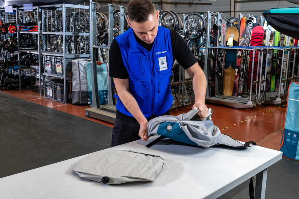 Delavec v trgovini Decathlon skrbno pregleduje kolo, medtem ko ga pripravlja za servis ali popravilo, pri tem pa uporablja specializirano orodje.