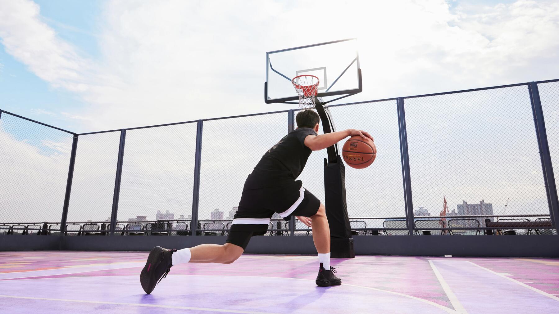 Junge springt mit rotem Basketball, trägt blaues Sportoutfit, grauer Hintergrund, dynamische Pose.