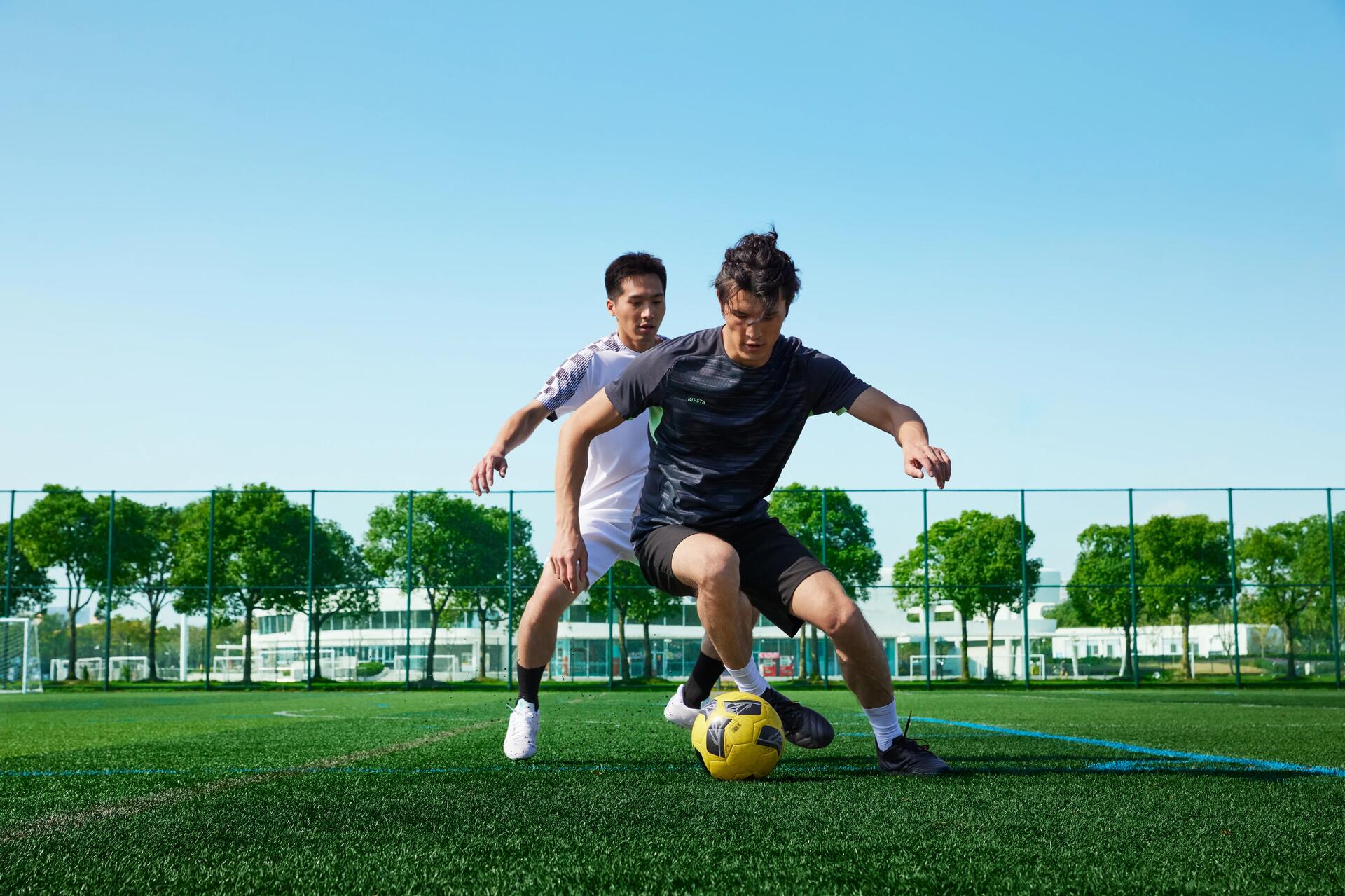 2 voetballers die aan het voetballen zijn. 1 voetballer probeert weg te dribbelen van de ander.