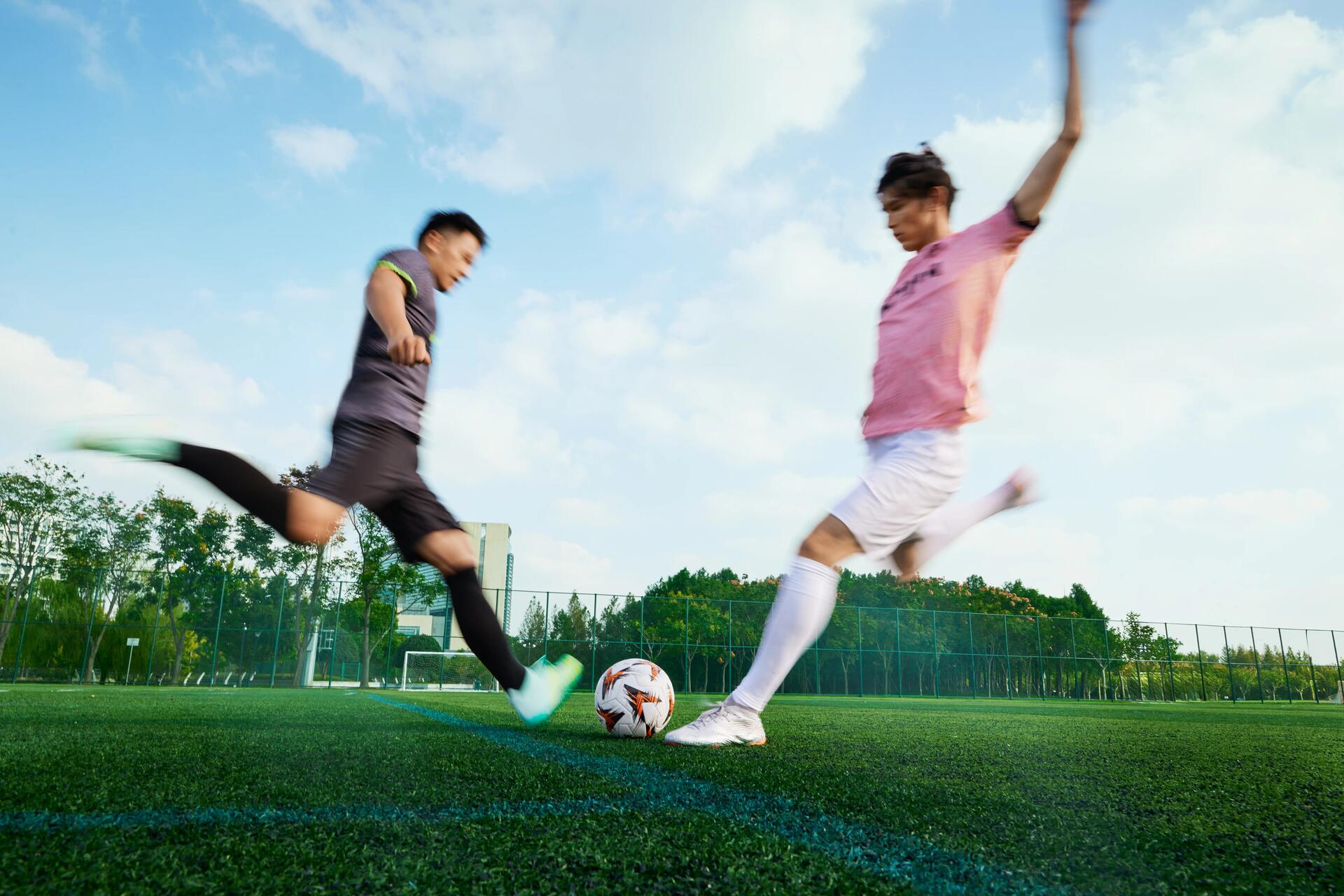 2 voetballers die vol voor de bal gaan tijdens een duel
