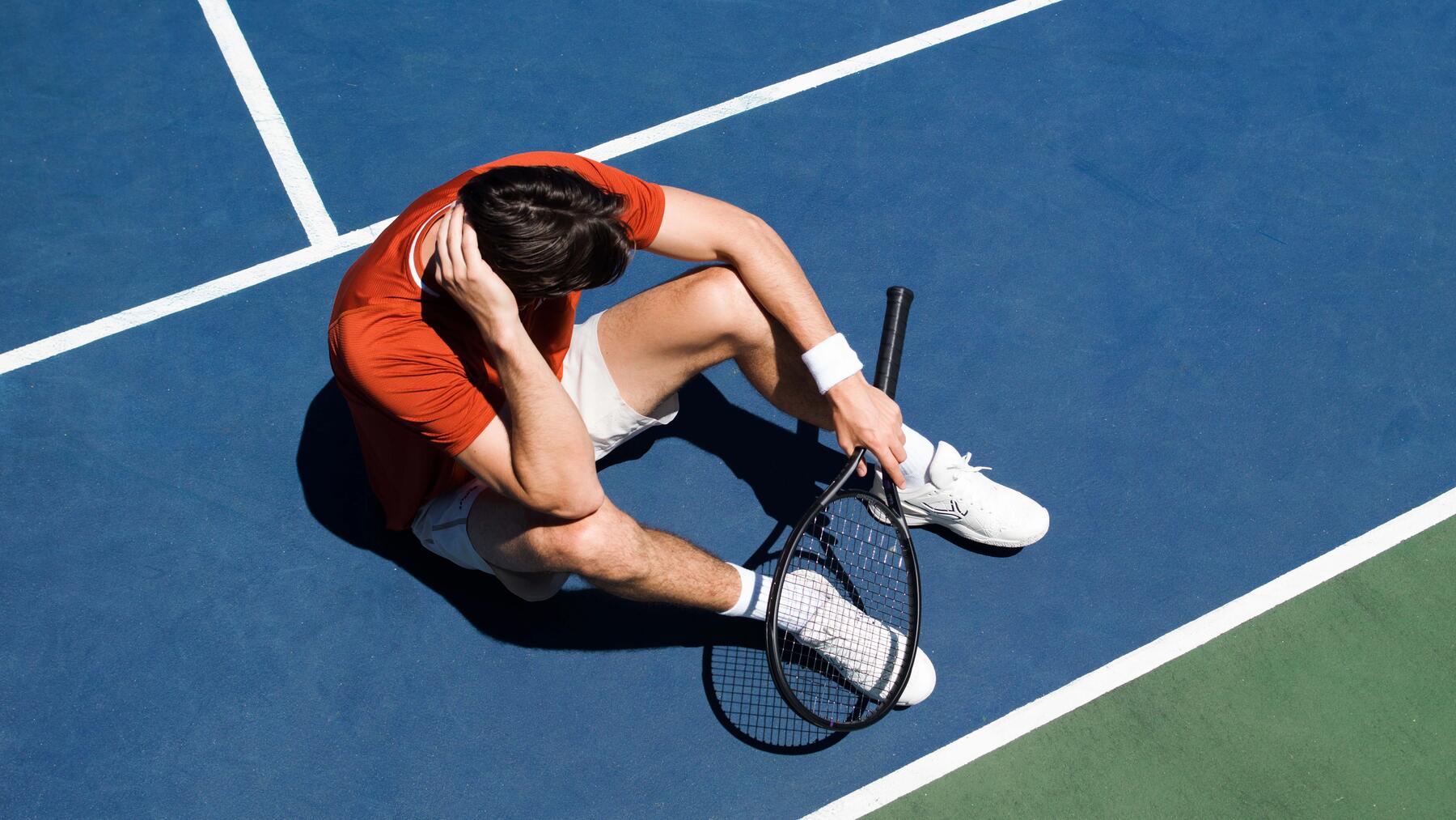 Mann sitzt mit Tennisschläger auf dem Platz