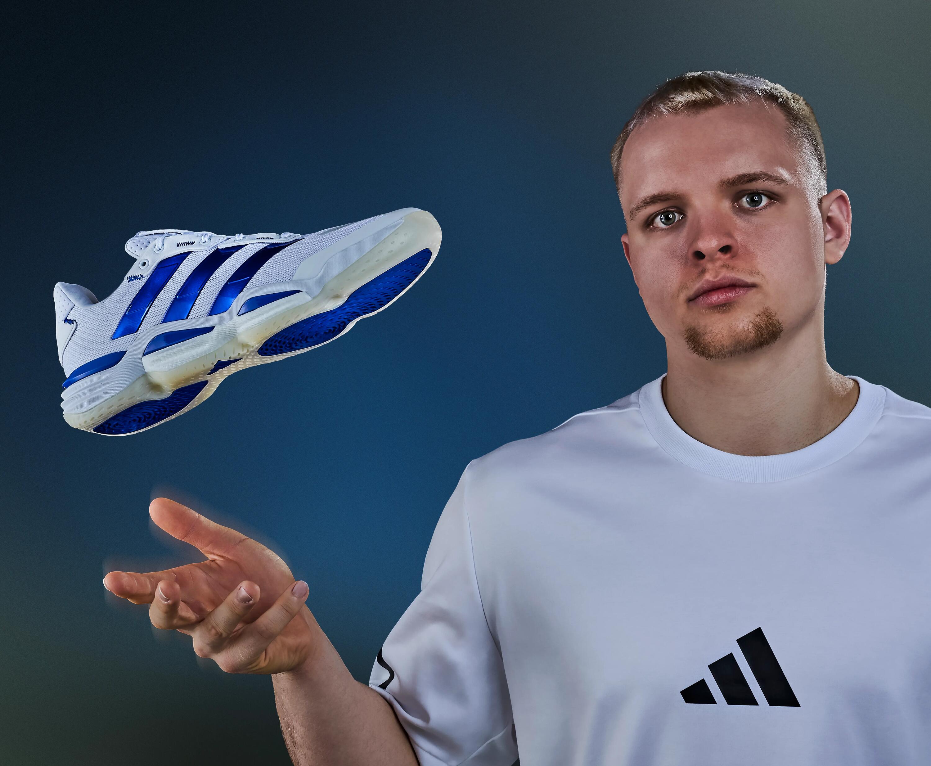 Mann hält adidas Stabil 16 Schuh zwischen seinen Händen und schaut in die Kamera.