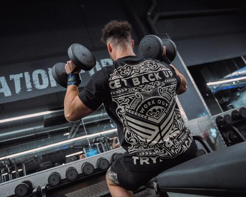 Mężczyzna w odzieży sportowej trenujący ze sprzętem do crossfitu siedząc na ławeczce do ćwiczeń