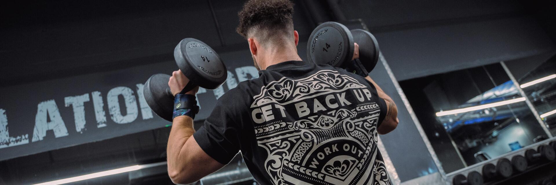 Mężczyzna w odzieży sportowej trenujący ze sprzętem do crossfitu siedząc na ławeczce do ćwiczeń