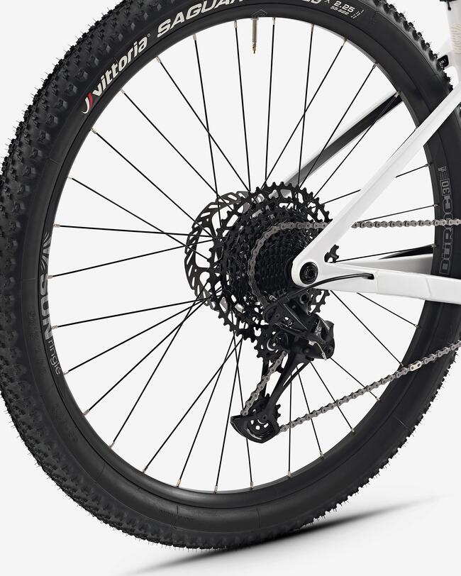 Schwarzes Fahrrad-Hinterrad mit grobem Profil, weißem Rahmen, vielen Speichen und sichtbaren Metallzahnrädern.