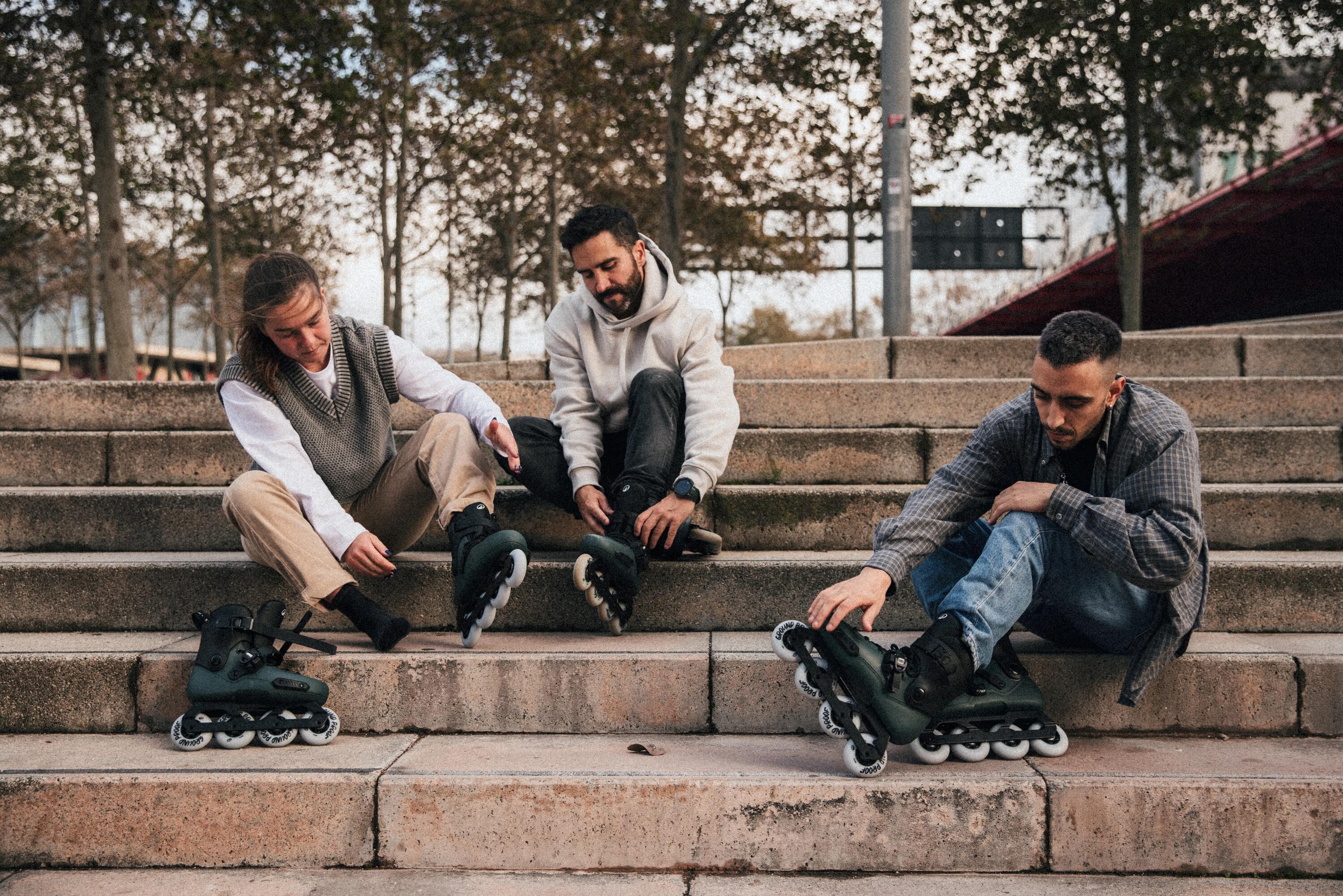 Vier Menschen fahren mit Inlineskates, Helmen und Schutzausrüstung auf einem sonnigen, von Bäumen gesäumten Parkweg.