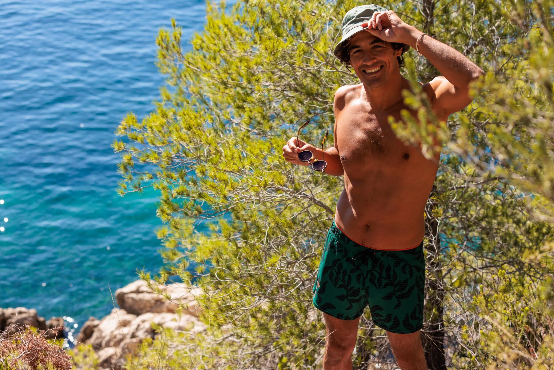 Mann steht am Mittelmeer in grüner Badehose für Herren