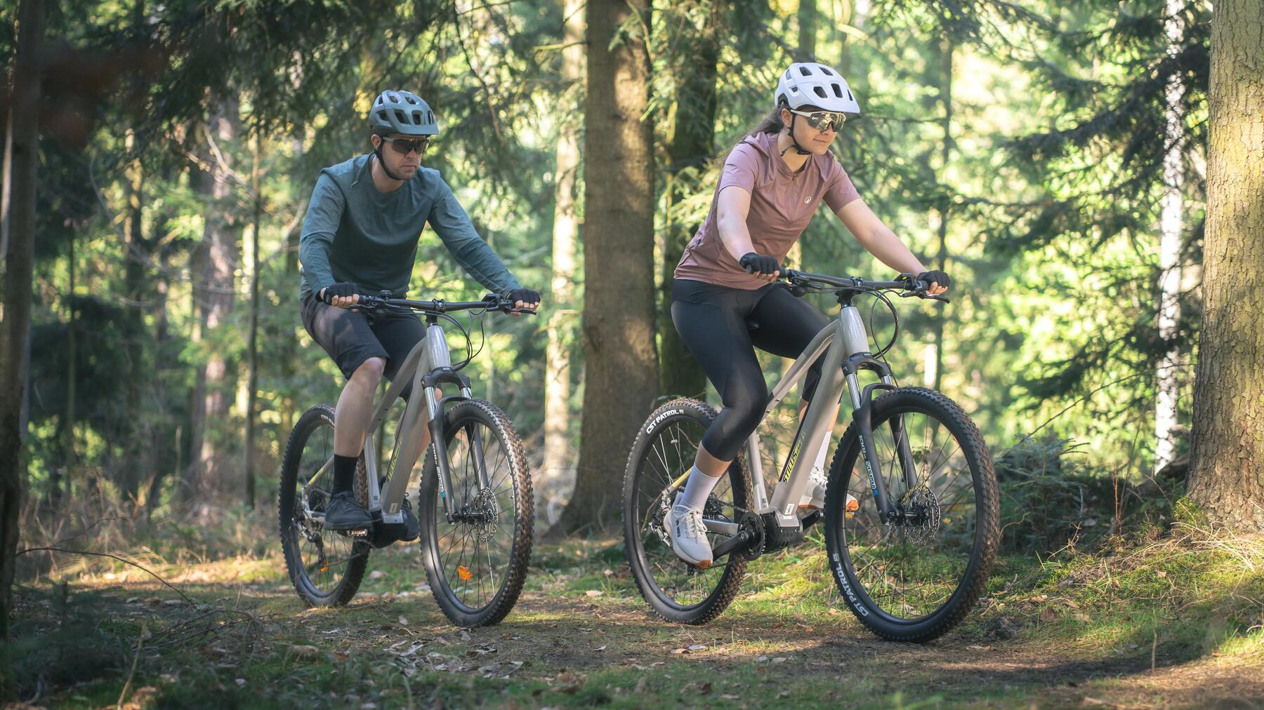 Kobieta i mężczyzna w kaskach rowerowych jadący na rowerach elektrycznych przez las