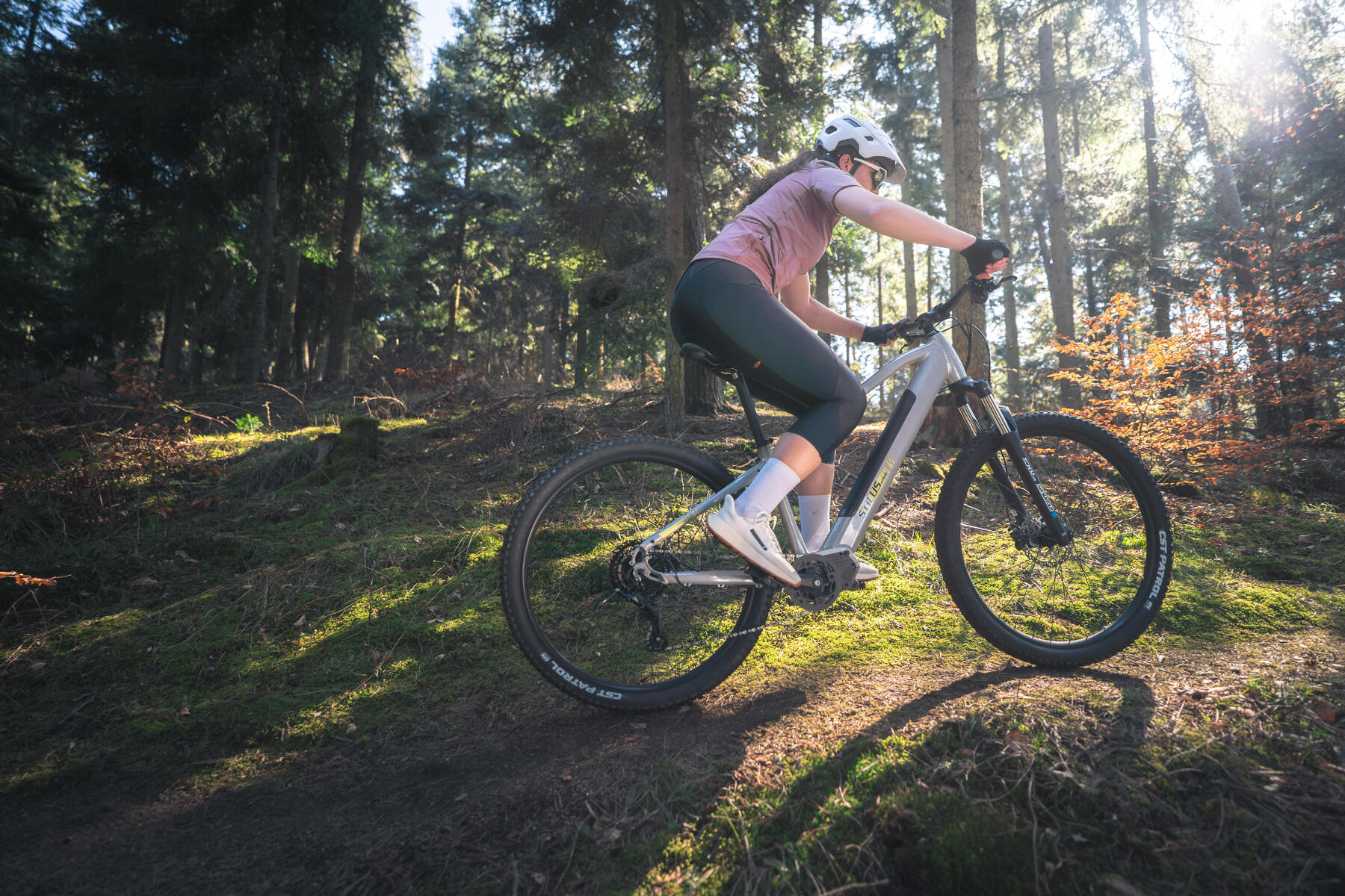 Kobieta w kasku i w okularach rowerowych jadąca na rowerze elektrycznym w lesie