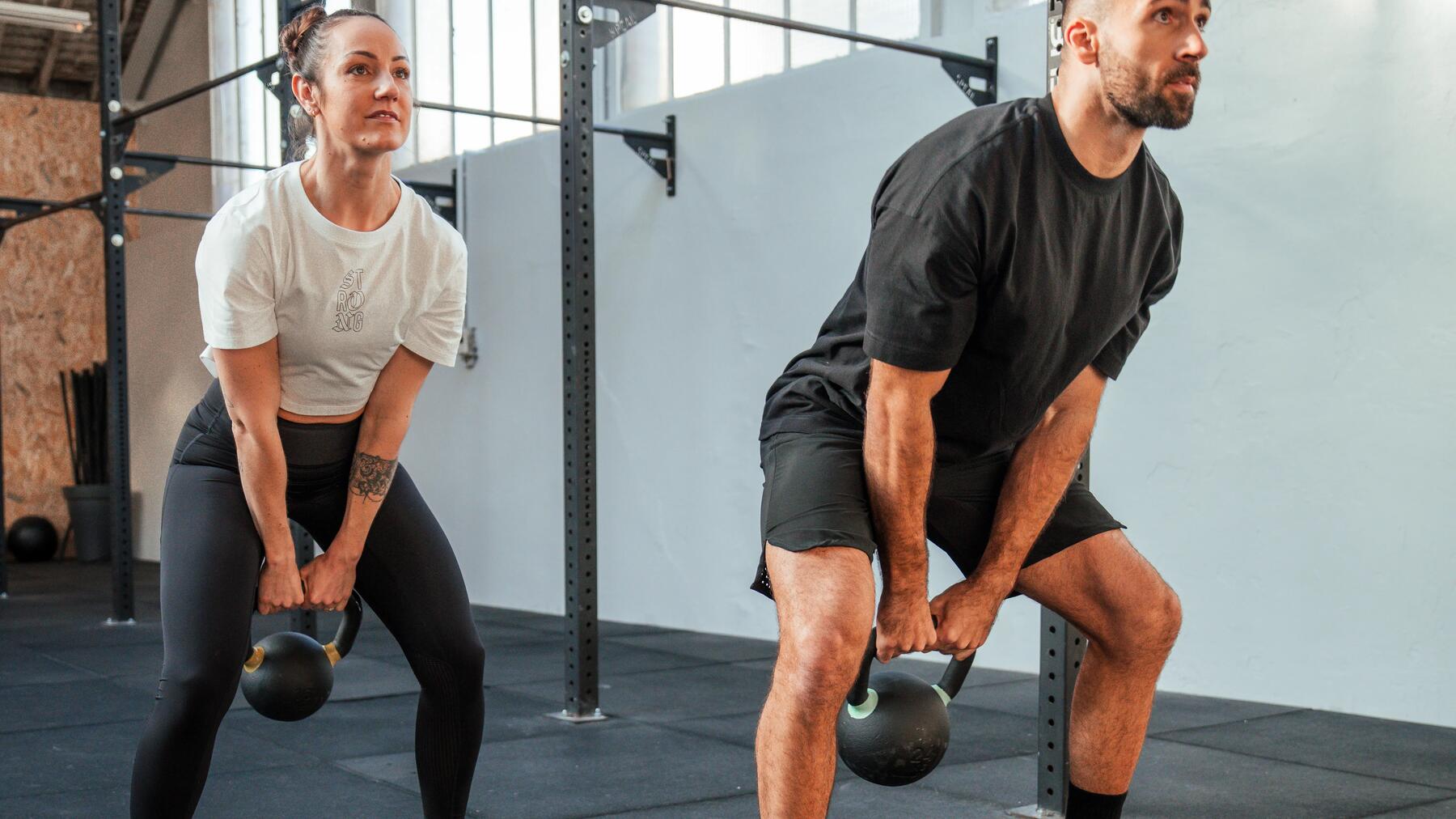 Kobieta z mężczyzną ćwiczący przysiady z kettlebellem w rękach na siłowni